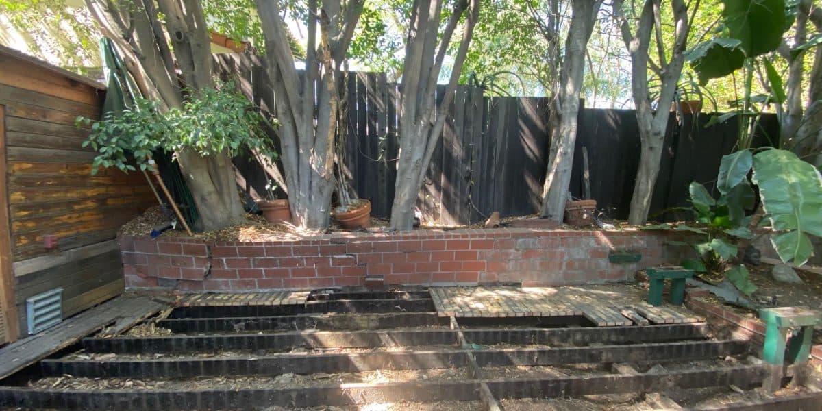 Cracked brick planter wall with rotted wooden decking beneath it